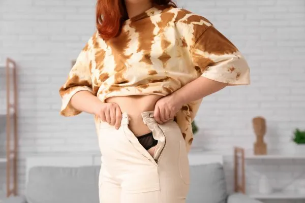 Image of woman trying to do her trousers up after pregnancy weight gain Cookham