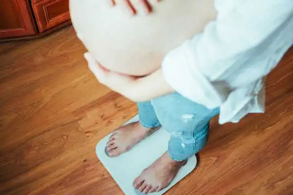 Image of woman weighing herself and experiencing weight gain through pregnancy Cookham